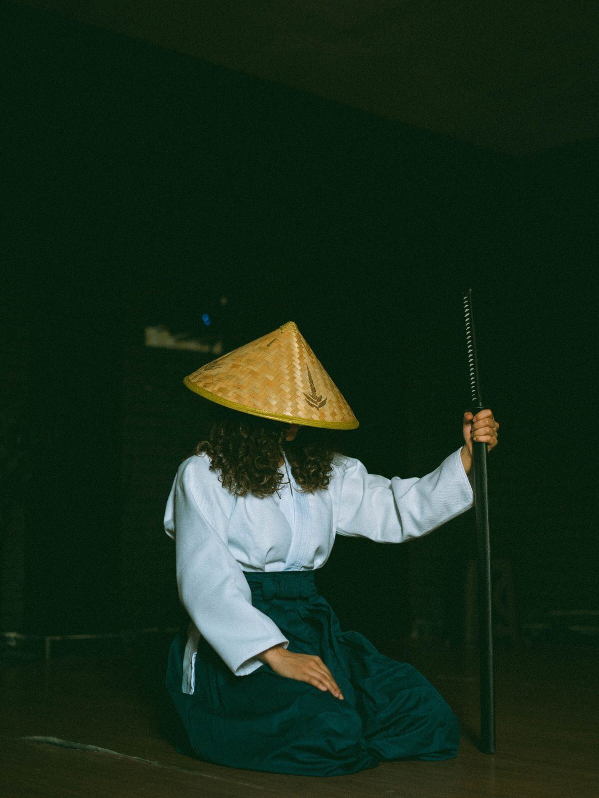 A lone figure in a straw hat kneeling in the dark