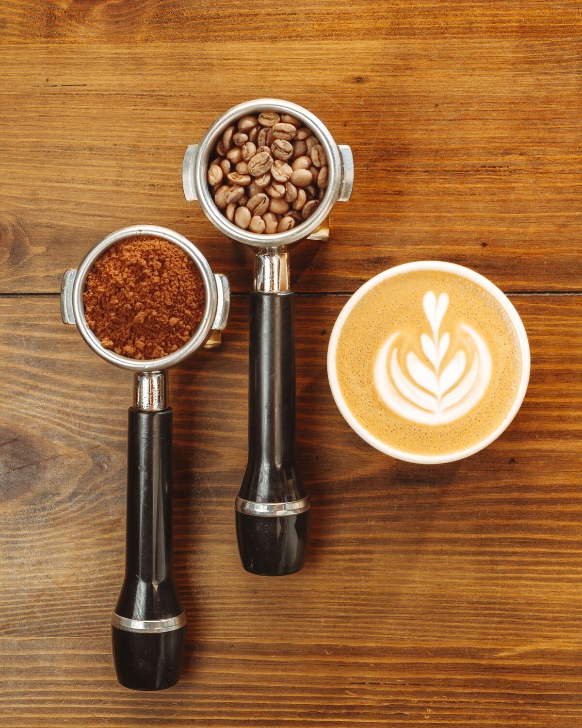 An espresso portafilter beside a latte with leaf art