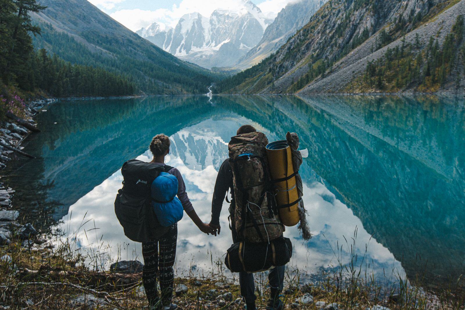 Two hikers with backpacks beside a turquoise mountain lake