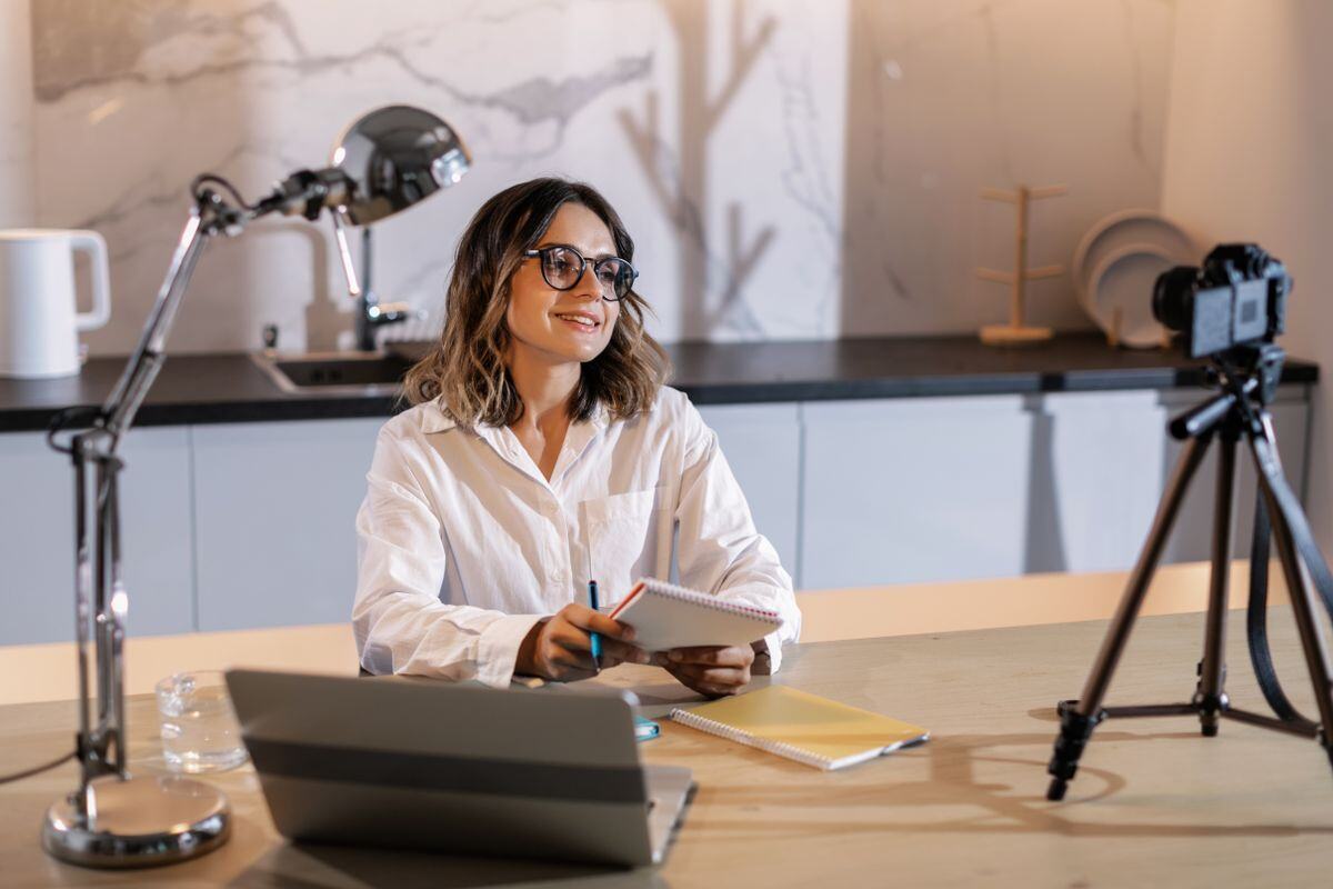 A woman filming herself at a desk with a phone on a tripod