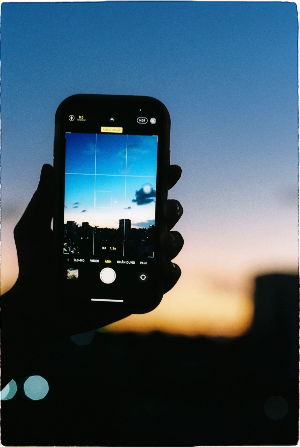 A hand holding up a phone against a dusk sky