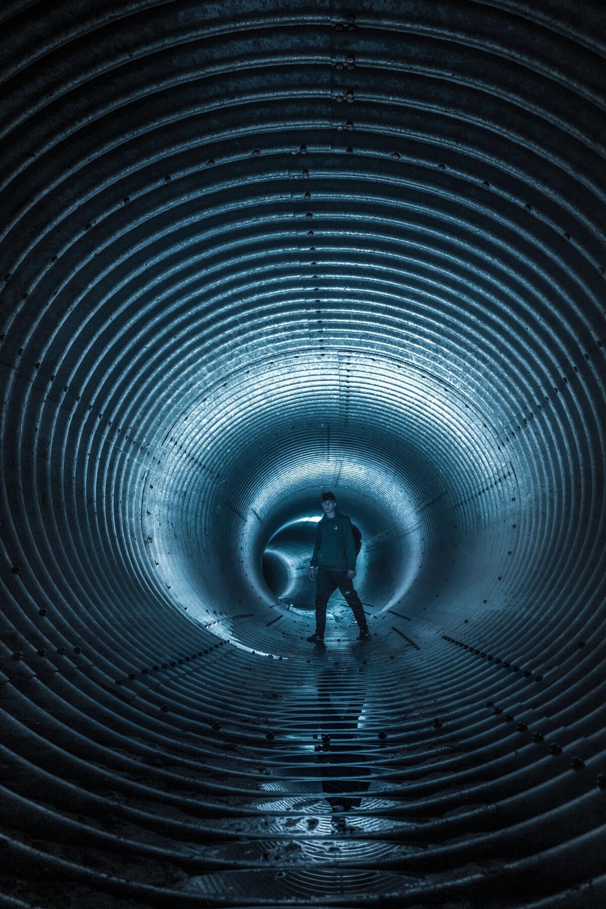 A figure walking through a long tunnel lit in cold blue
