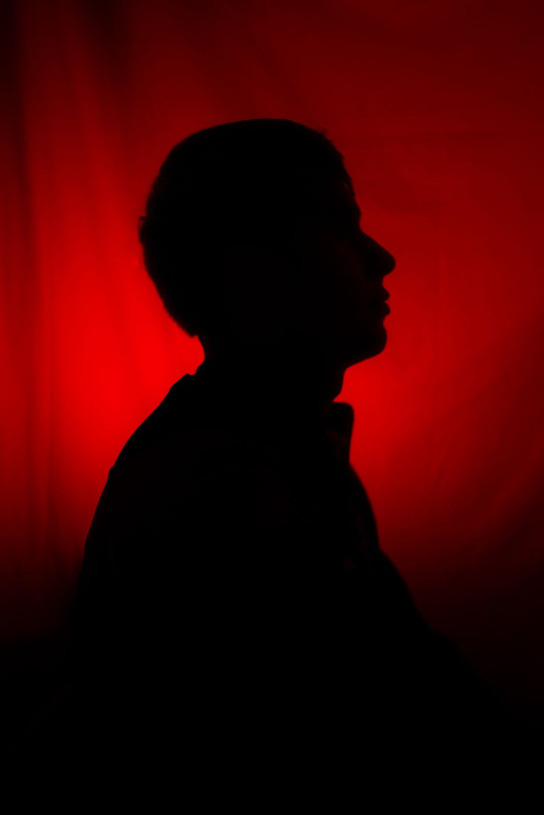 Silhouette of a person in profile against a red backdrop