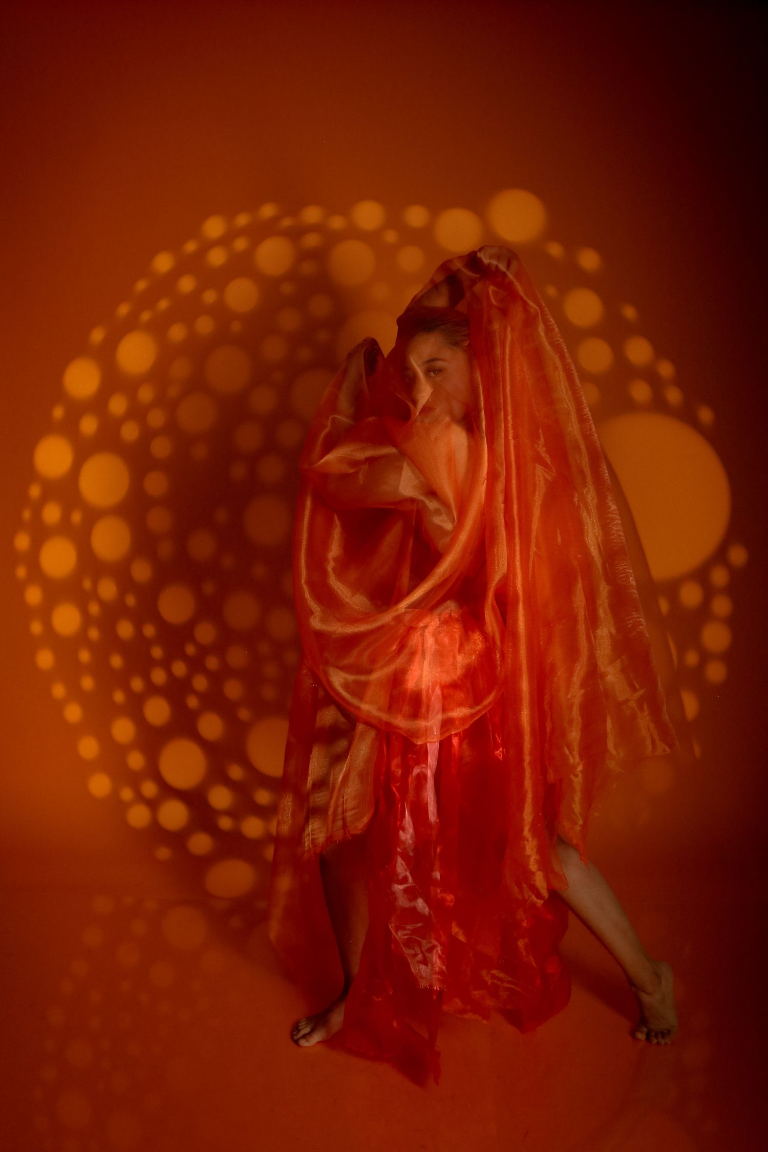 A dancer wrapped in flowing orange fabric under dramatic light