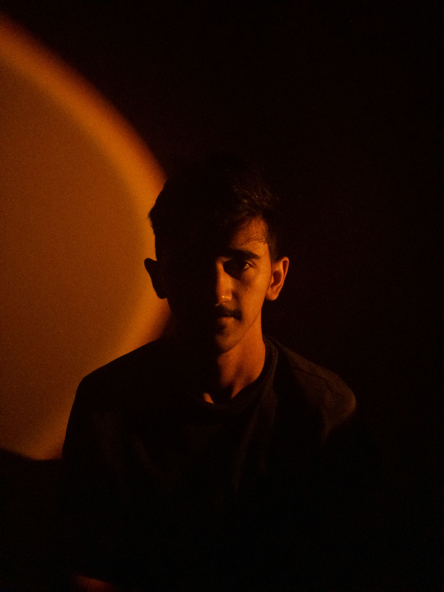 A man’s face lit by warm orange light against a dark background