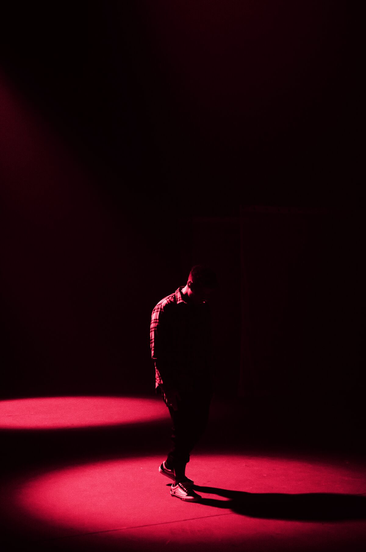 A figure in a pool of red light on a dark stage