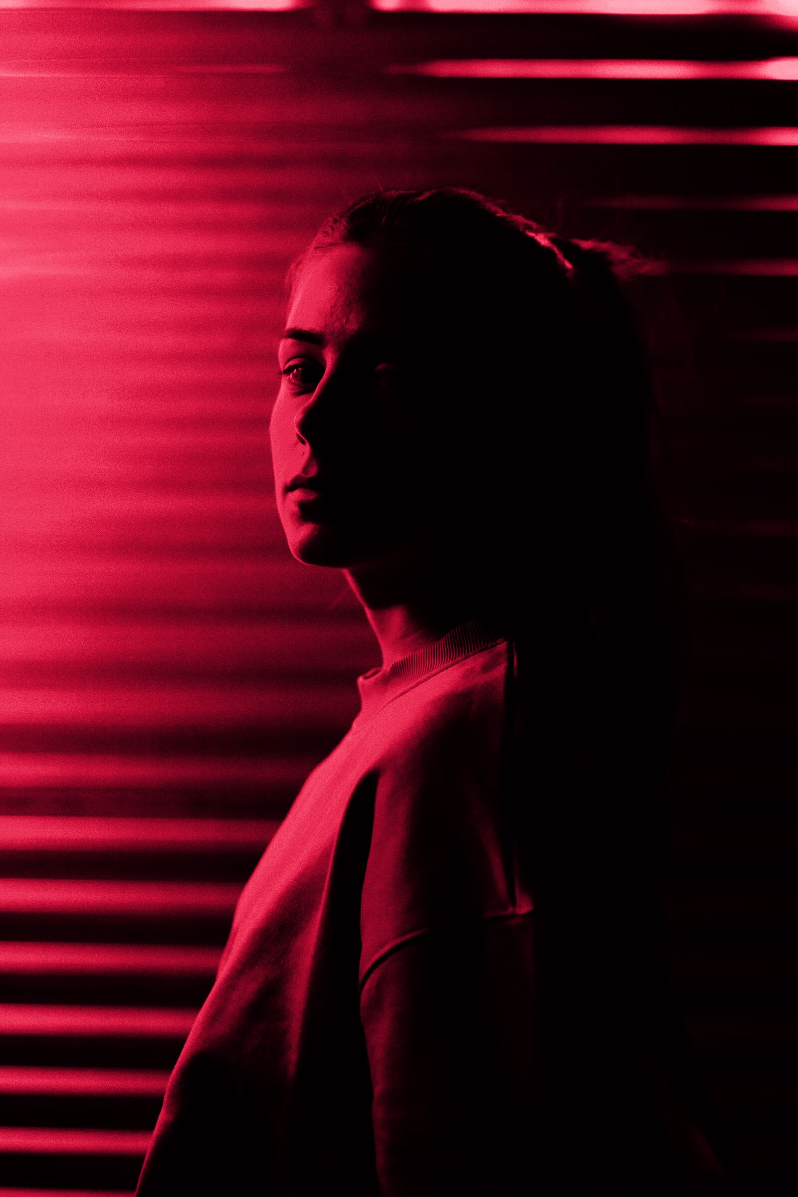 A woman in red light through window blinds
